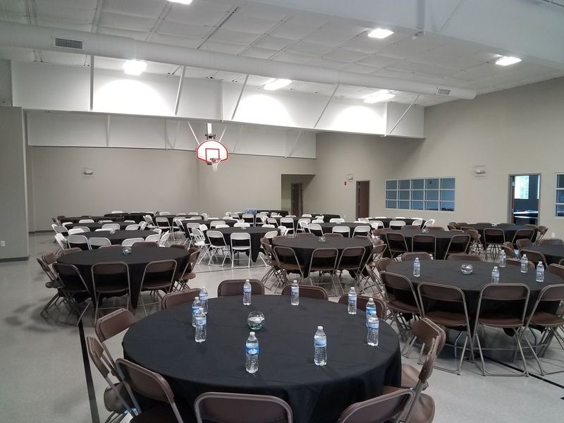 The second-floor hall set with round tables, black tablecloths and water bottles, with a basketball hoop on the far wall.